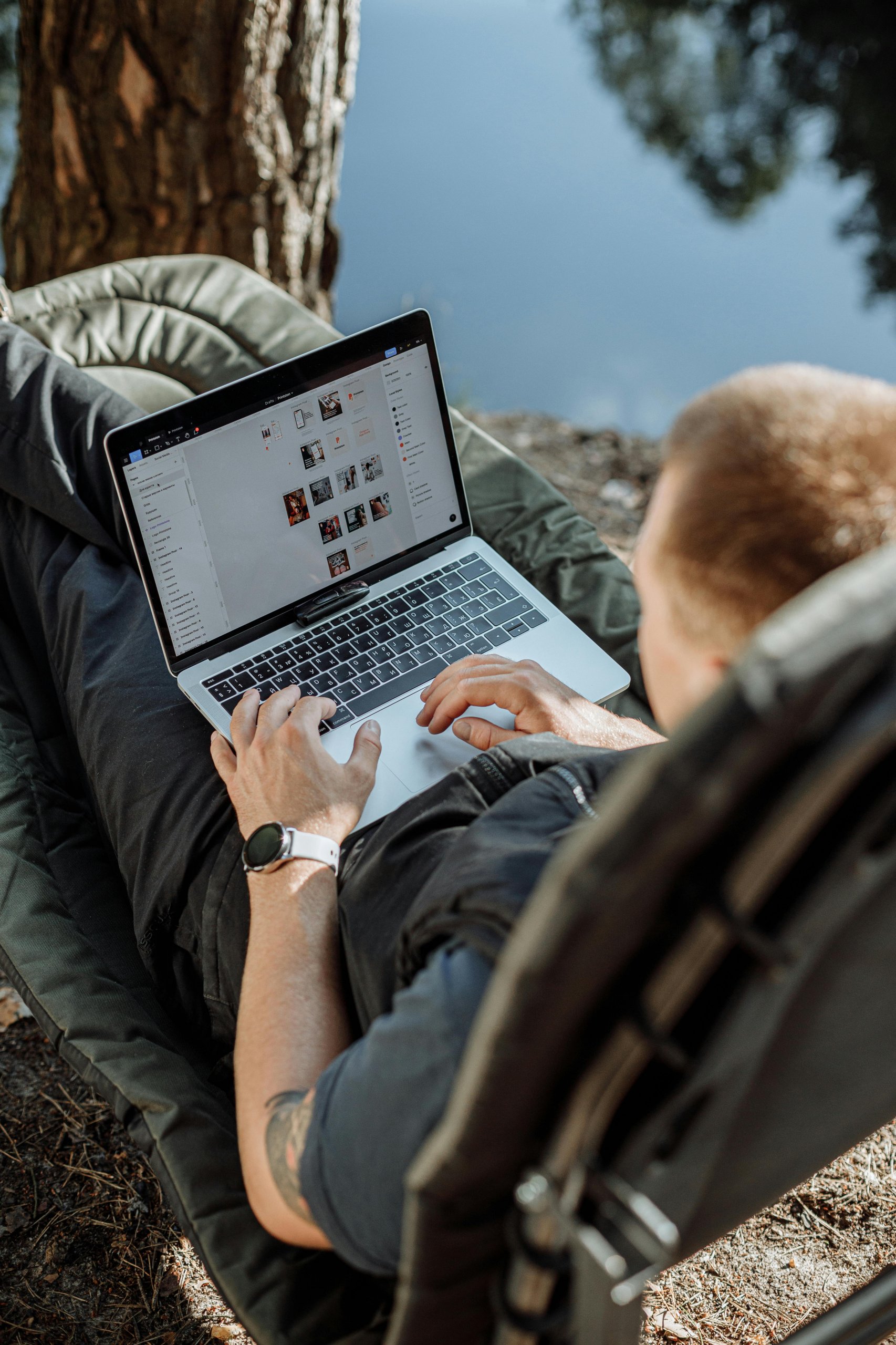 freedom-of-laptop-lifestyle man with open laptop sitting in ahammock close to river